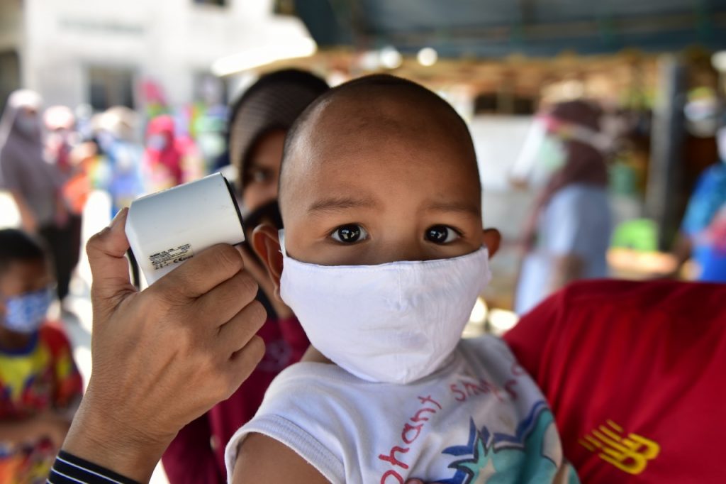 A young child wearing a face mask has a temperature check 